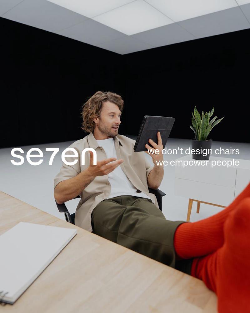 Man met een tablet op een Se7en-stoel, advertentie "we don't design chairs, we empower people"