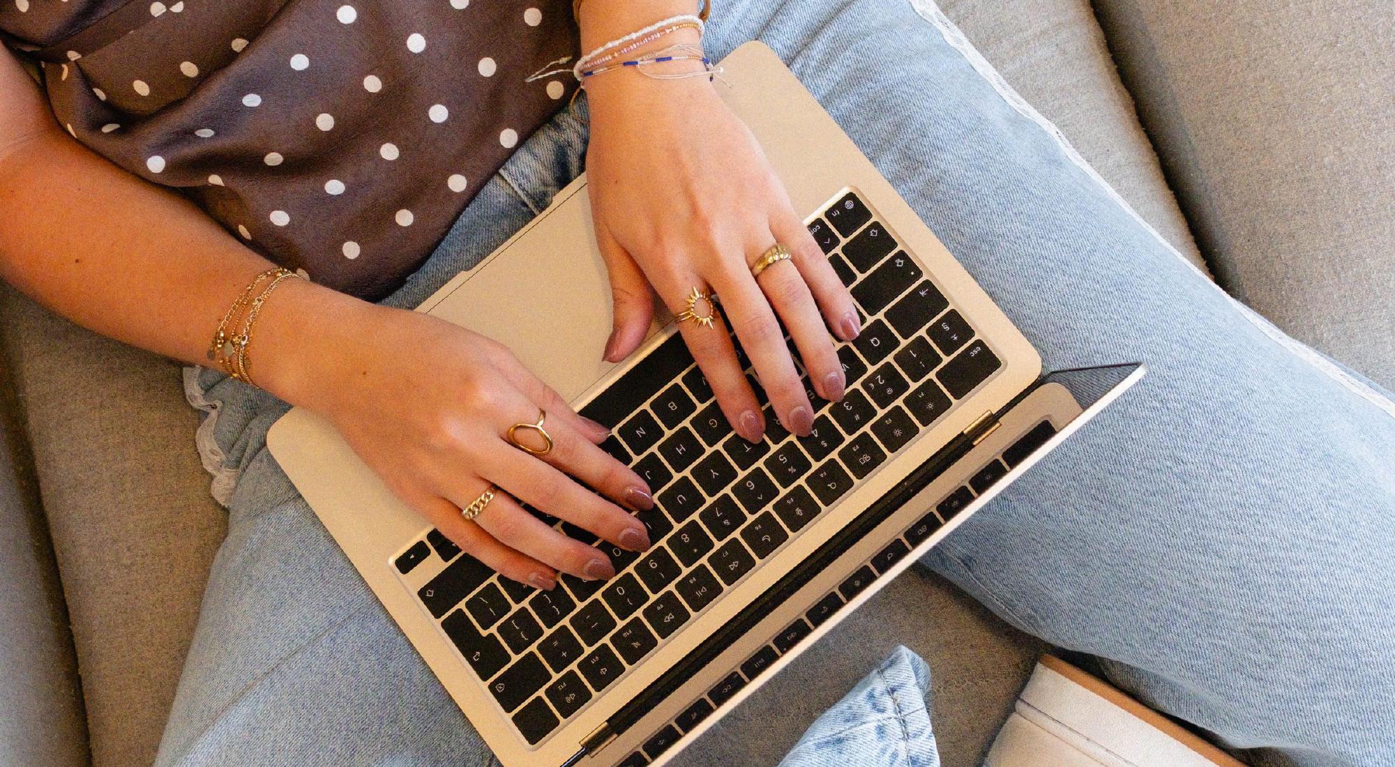 Iemand typt op een laptop op een lichtgrijze bank