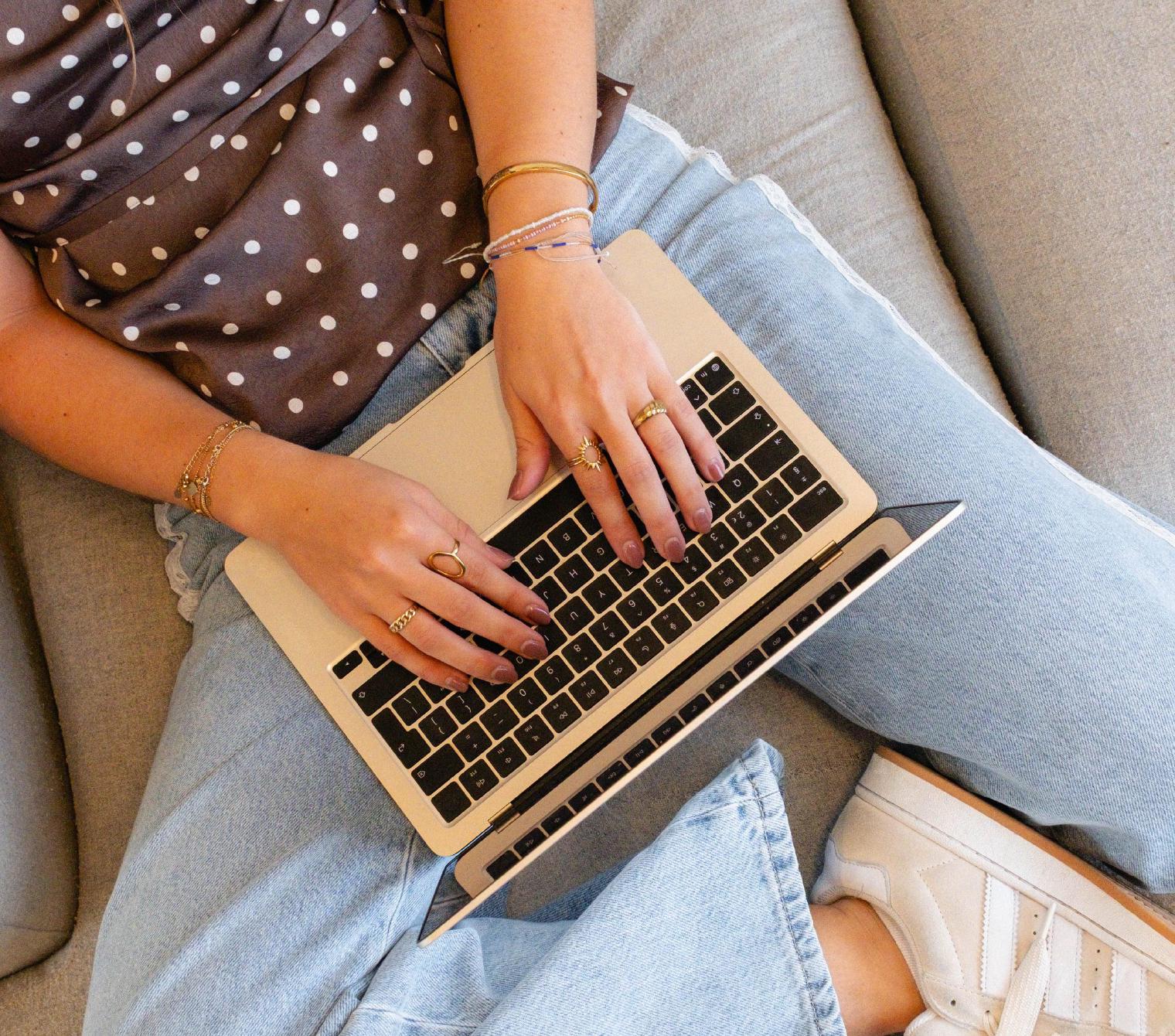 Iemand typt op een laptop op een lichtgrijze bank