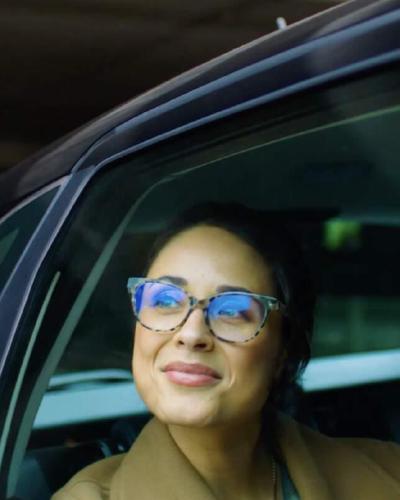 Lachende vrouw met bril kijkt uit het raam van een auto, beeld uit een campagne