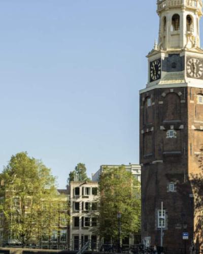 Amsterdamse Montelbaanstoren met een boot vol mensen op de gracht, beeld uit een campagne van Mokumboot