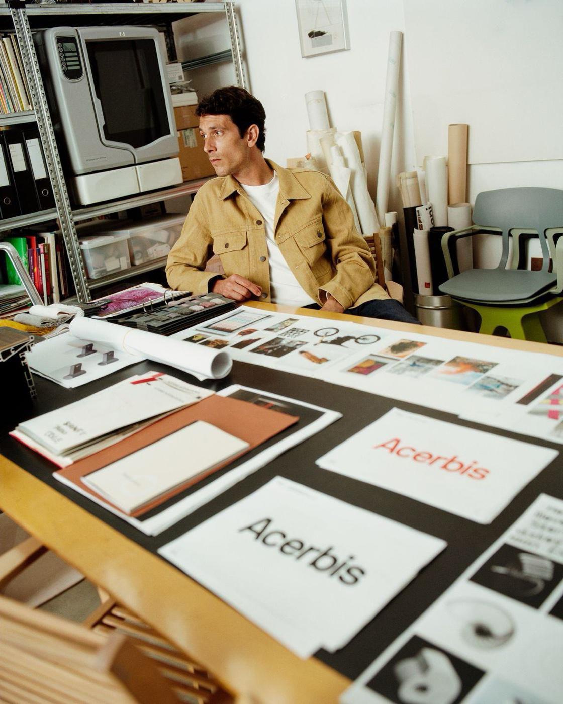 Ontwerper aan een studiotafel vol merkconcepten en drukwerk