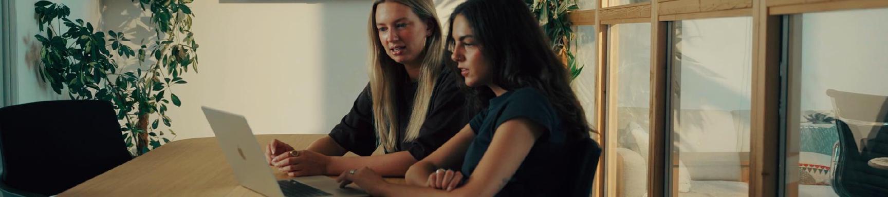 Twee collega's kijken samen naar een laptop aan een vergadertafel