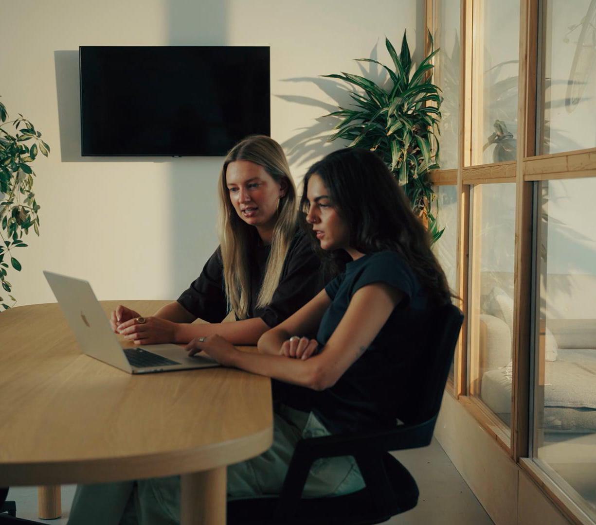 Twee collega's kijken samen naar een laptop aan een vergadertafel