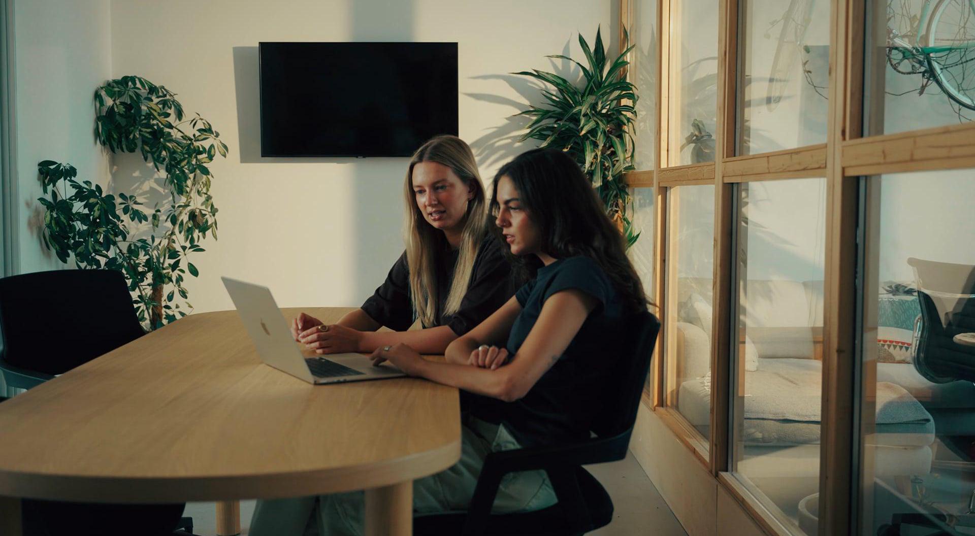Twee collega's kijken samen naar een laptop aan een vergadertafel